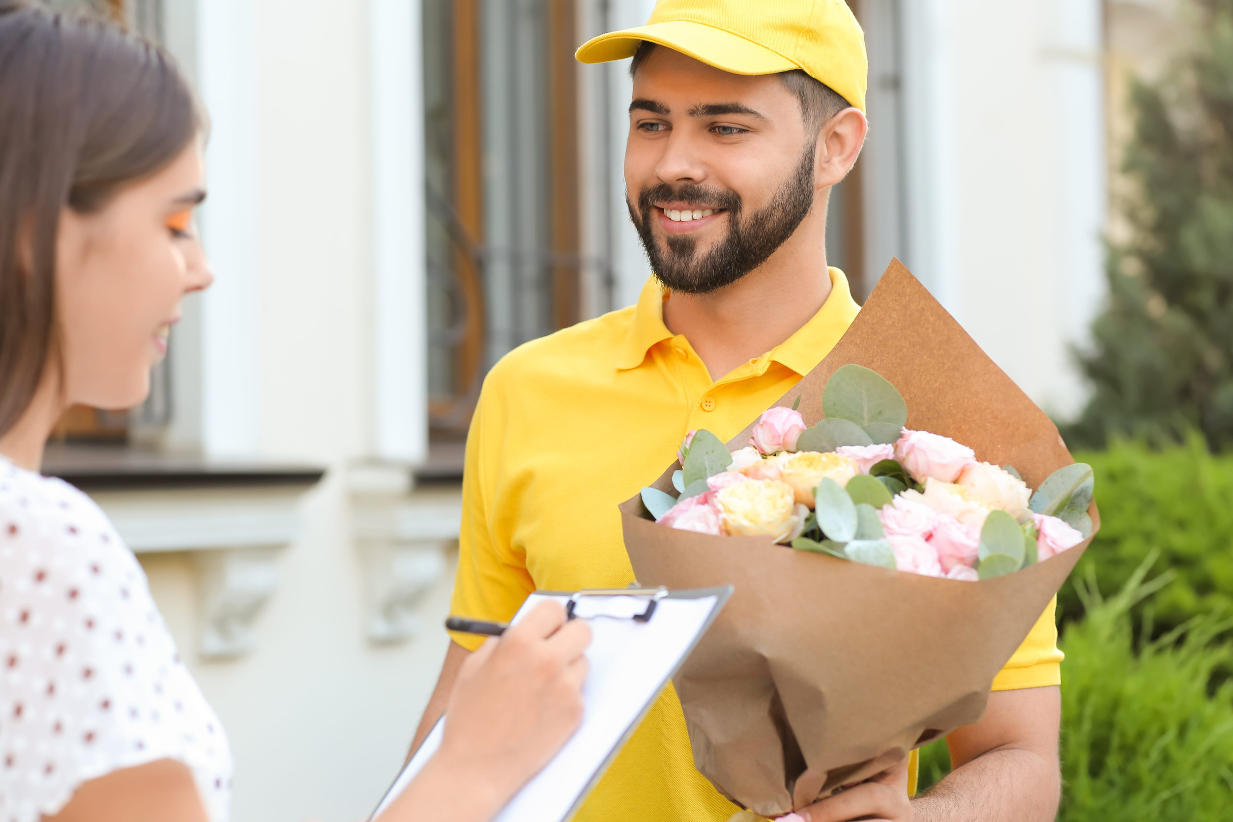 Young woman receiving flowers from courier outdoors