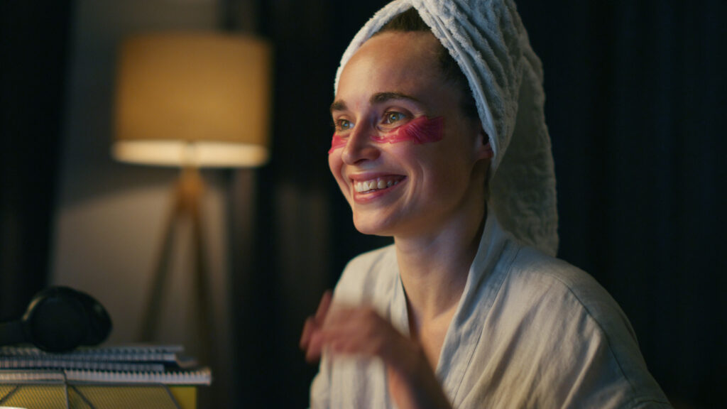 Happy girl waving hand closeup. Cheerful female professional making night video call at cozy apartments alone. Positive freelancer wearing bathrobe working chatting colleague at home evening