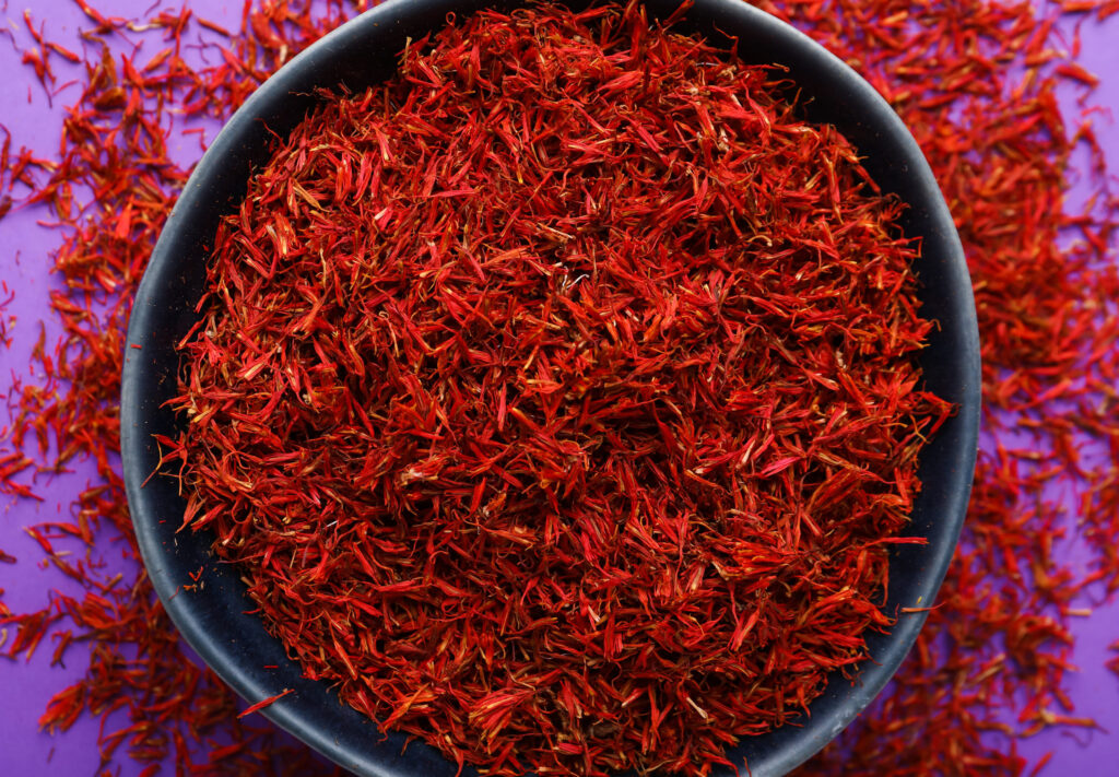 Bowl with pile of saffron on purple background