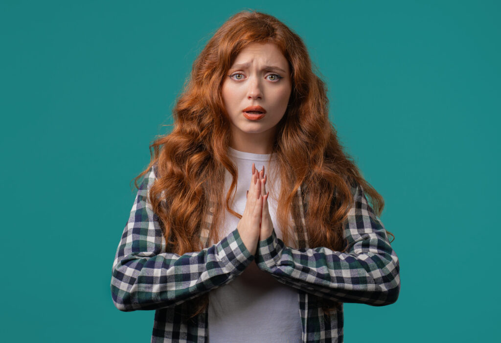 Young woman praying, begs to apologize her, she is guilty. Blue background. Hopeful prayer girl asking someone satisfy her desires, help with. High quality