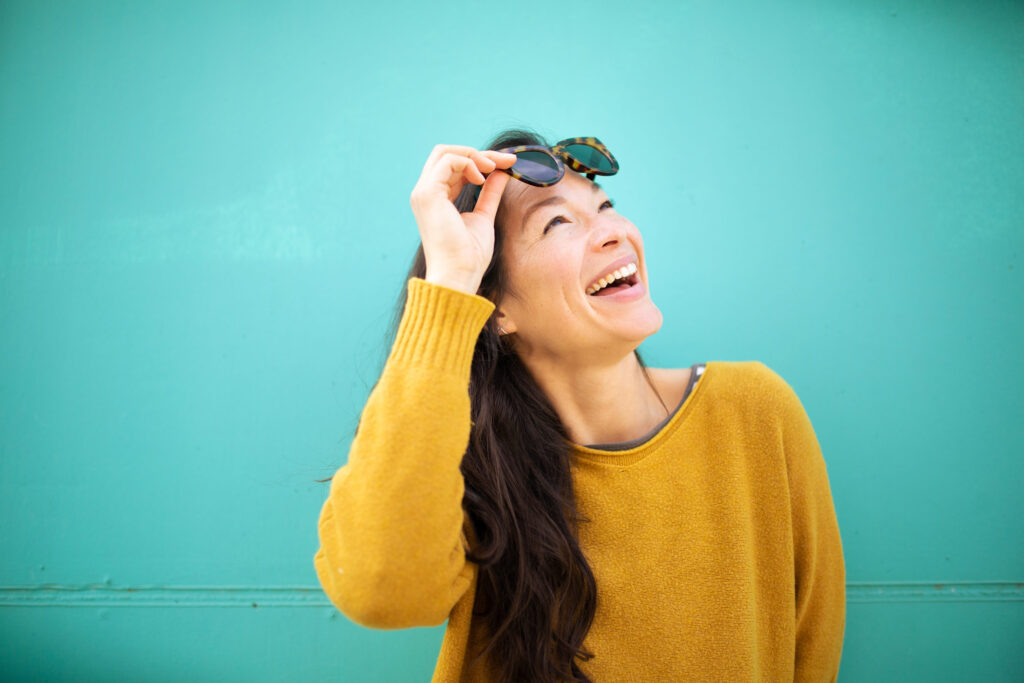 Close-up portrait of cheerful young asian woman with sunglasses looking away and smiling against green wall