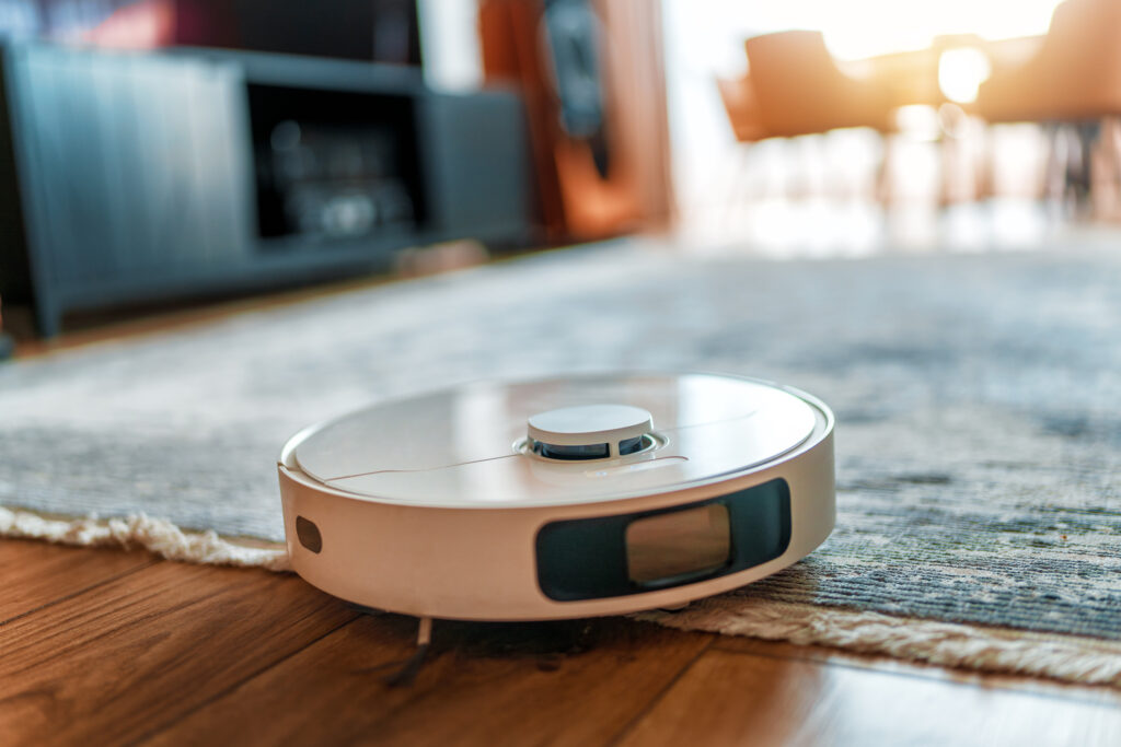 White robotic vacuum cleaner on wooden floor. Smart cleaning technolog