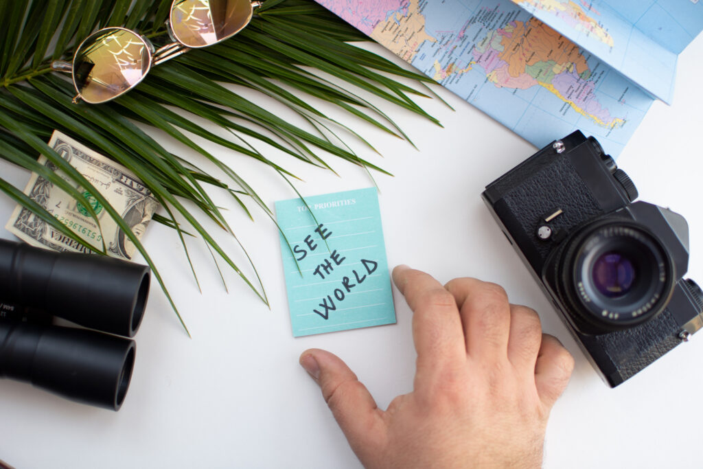 Travel planning concept. Top view of male hand, passport, camera, sunglasses and palm leaf on white background