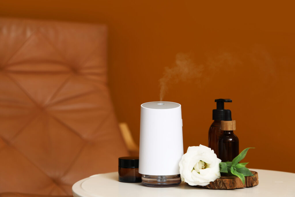 Air humidifier with essential oils and flower on table near orange wall in room