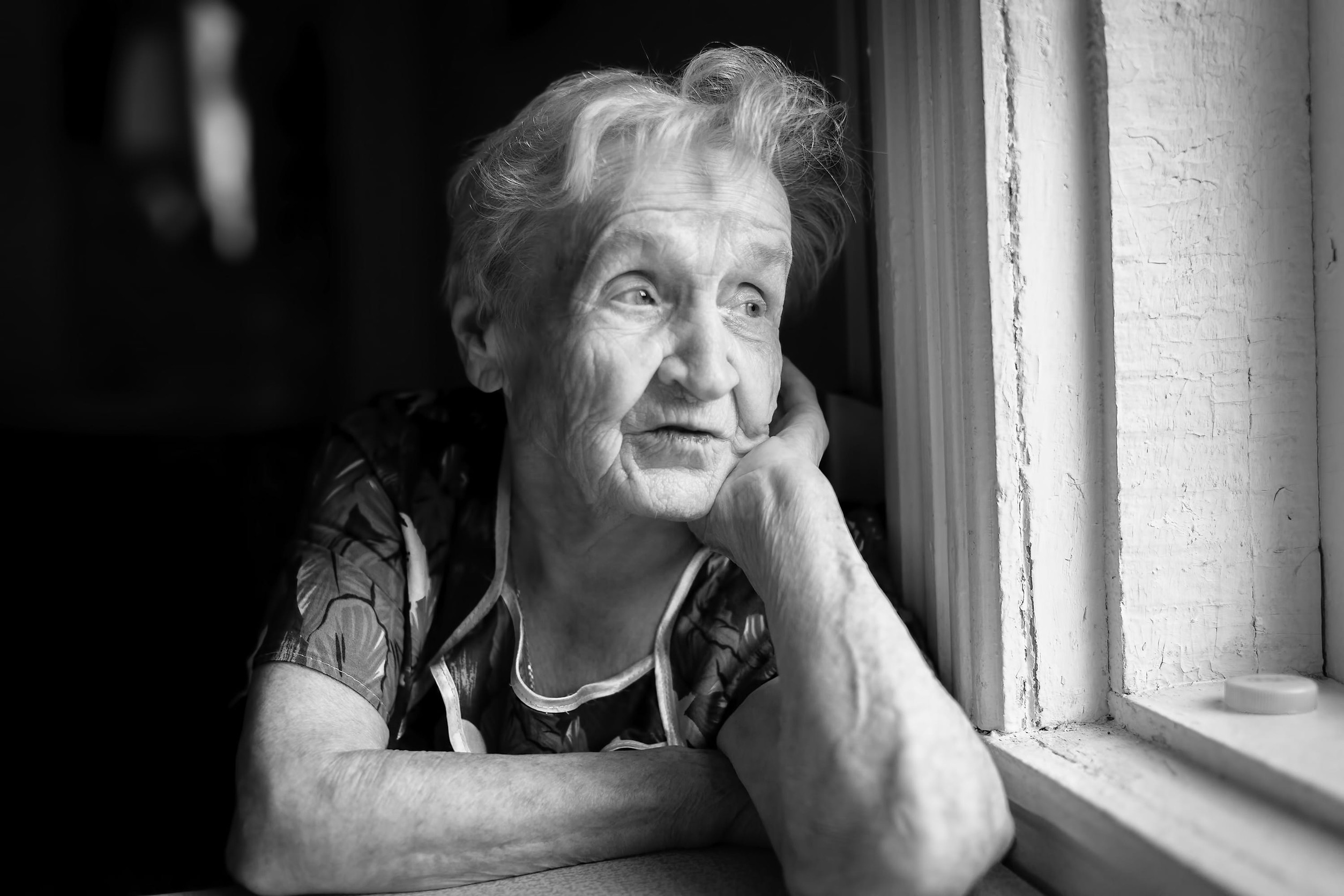 An elderly woman sitting near the window. Black-and-white photo.