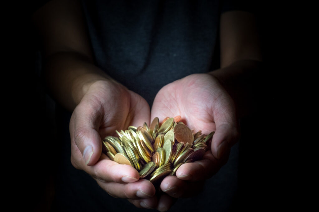 Male hand holding golden coins. Saving, money, finance donation, giving and bussiness concept. Black background. Heart shape.