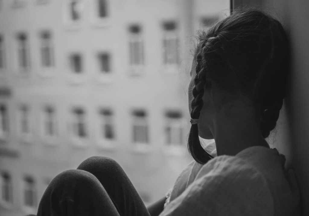 Sad little girl sitting near the window. Black and white