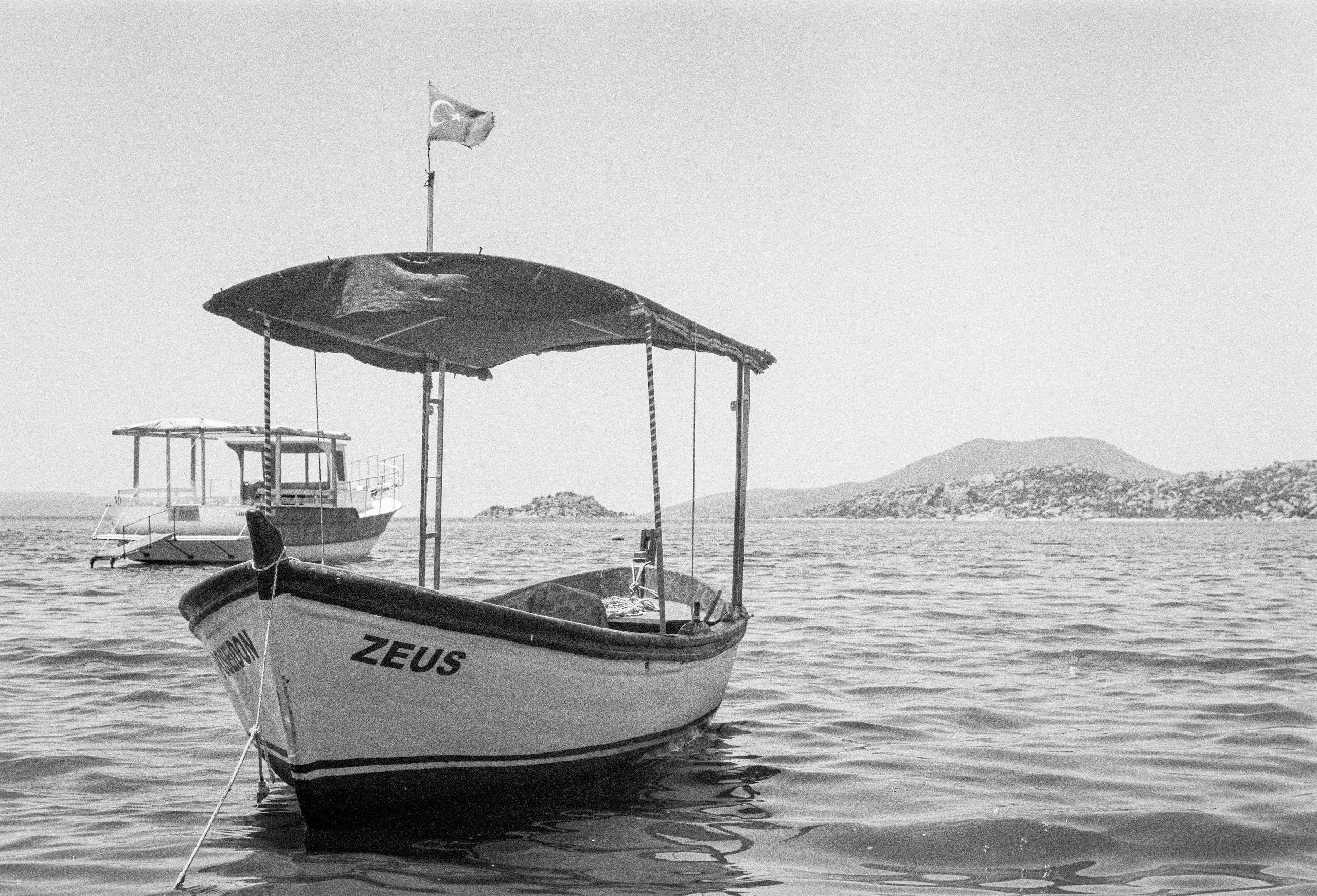 A black and white photo of a boat named Zeus with Turkish flag in calm waters.