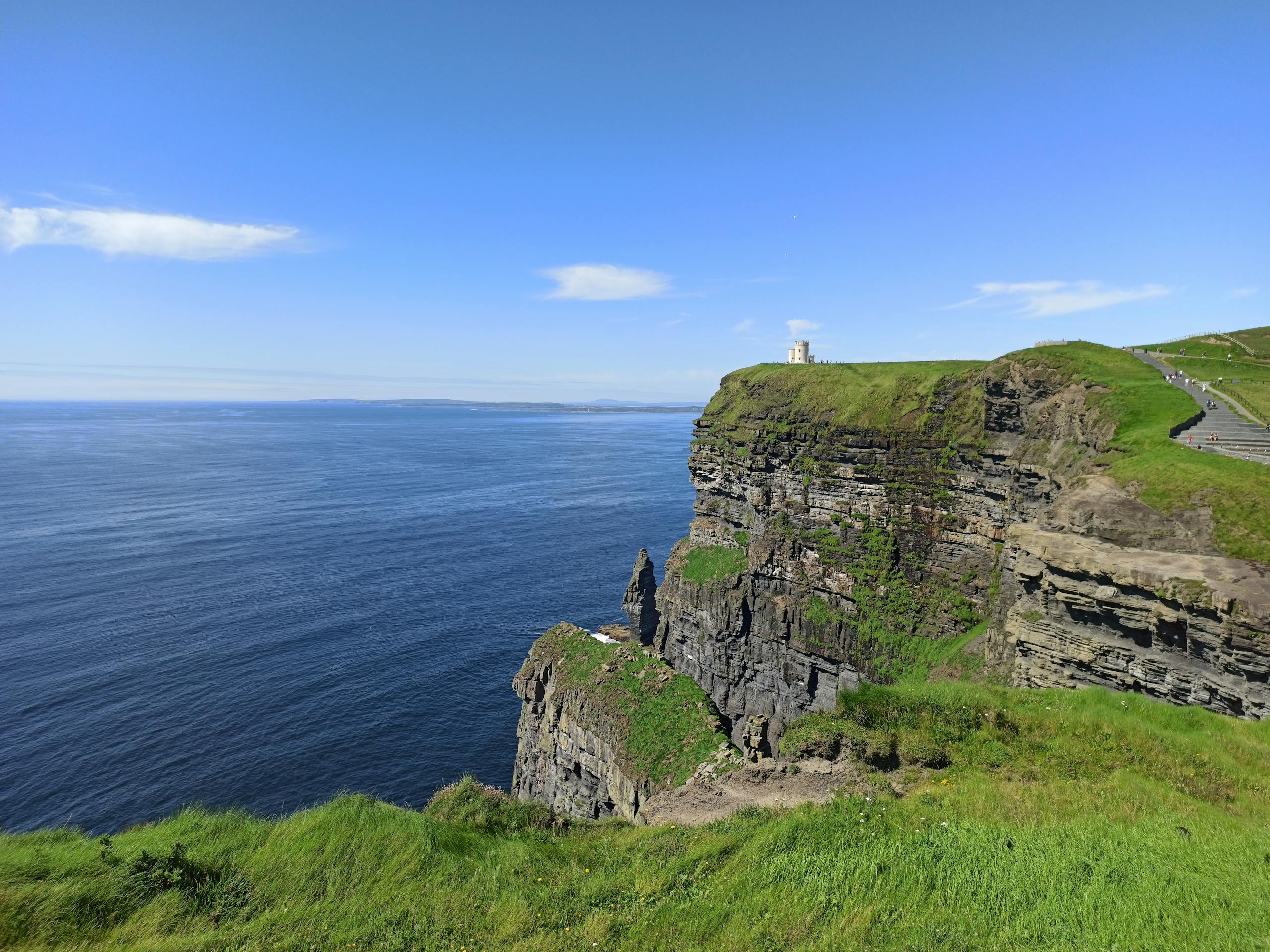 A breathtaking view of the Cliffs of Moher overlooking the Atlantic Ocean on a sunny day.