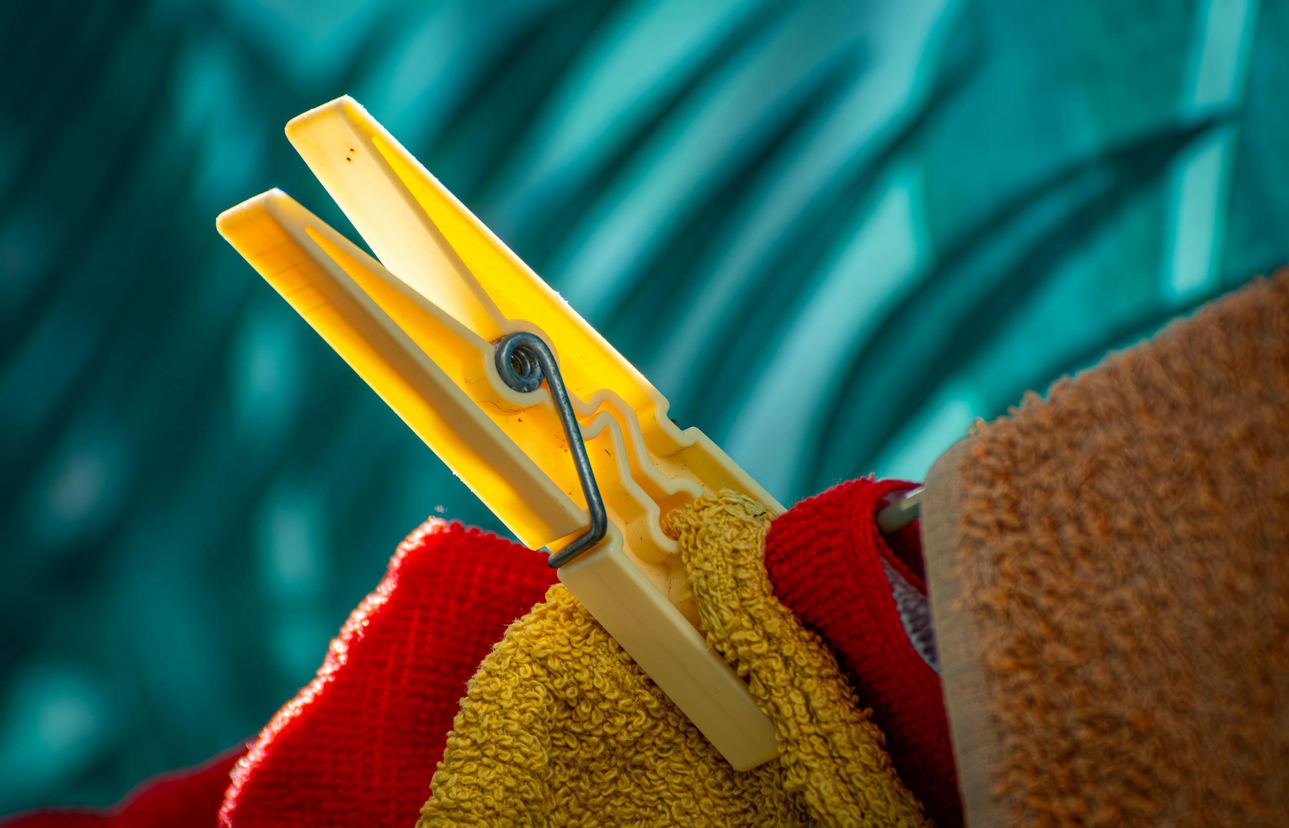 A bright yellow clothes peg clips colorful towels against a blurred blue background, creating a vivid contrast.