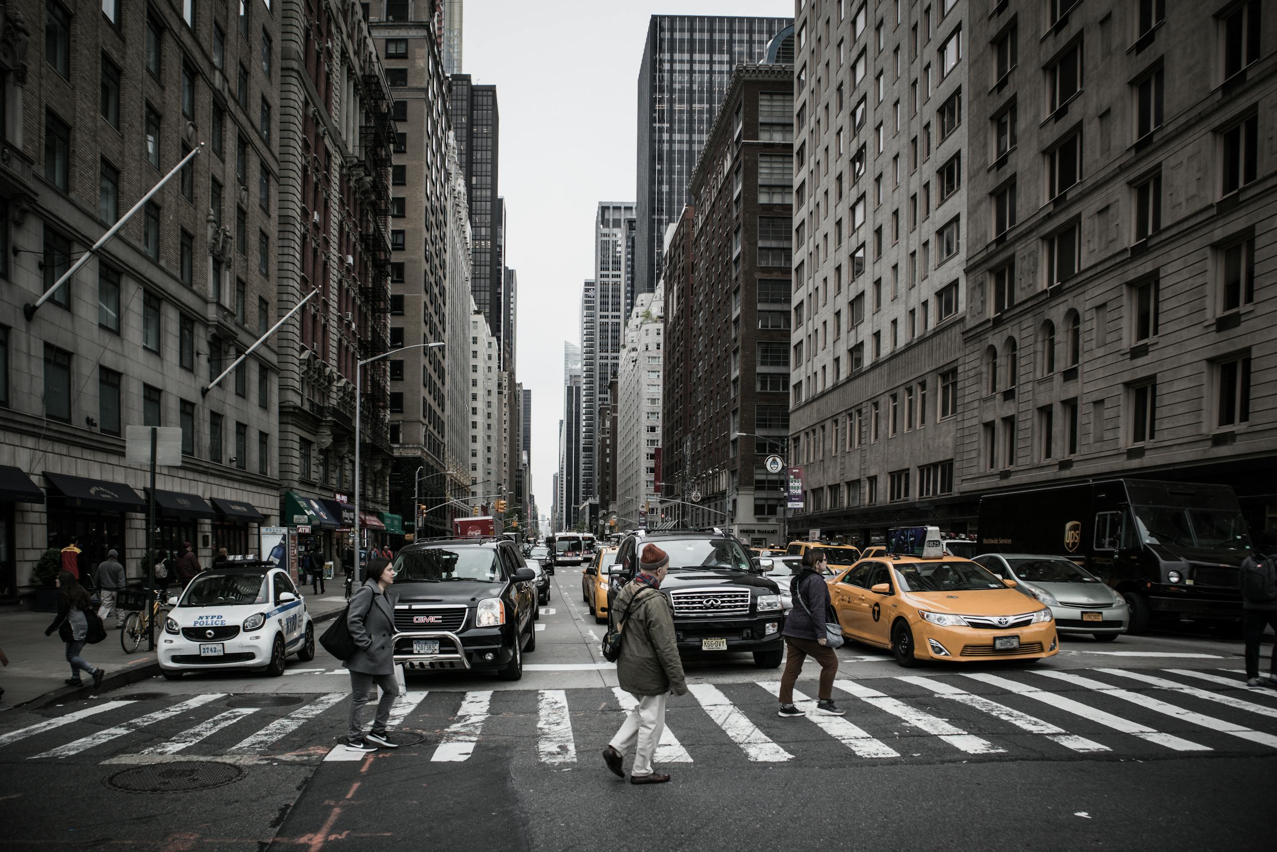 A bustling New York street view featuring pedestrians at a crosswalk amidst iconic yellow taxis and skyscrapers.
