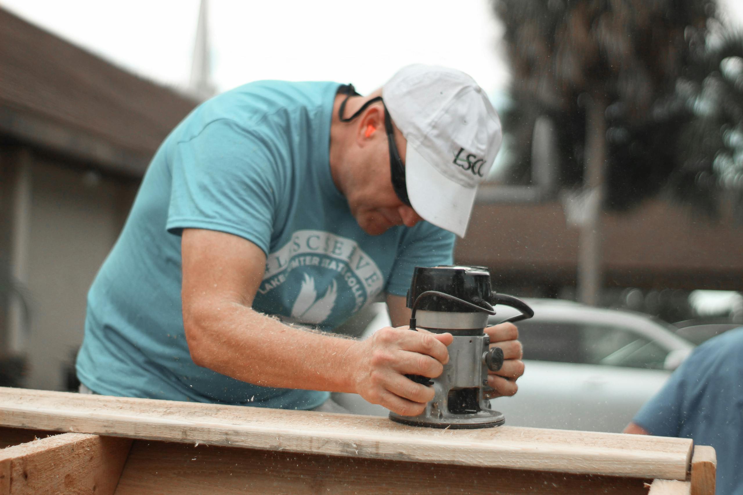 A carpenter uses a power tool to sand a wooden plank outdoors.