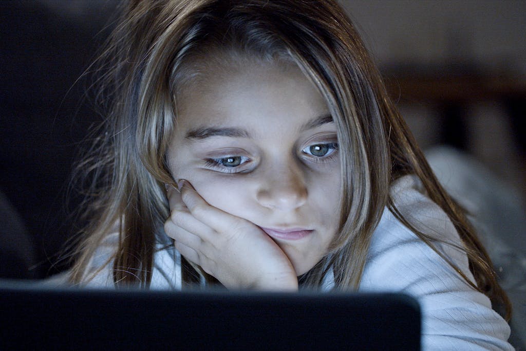 A child is focused on a laptop screen, absorbed in technology during nighttime.