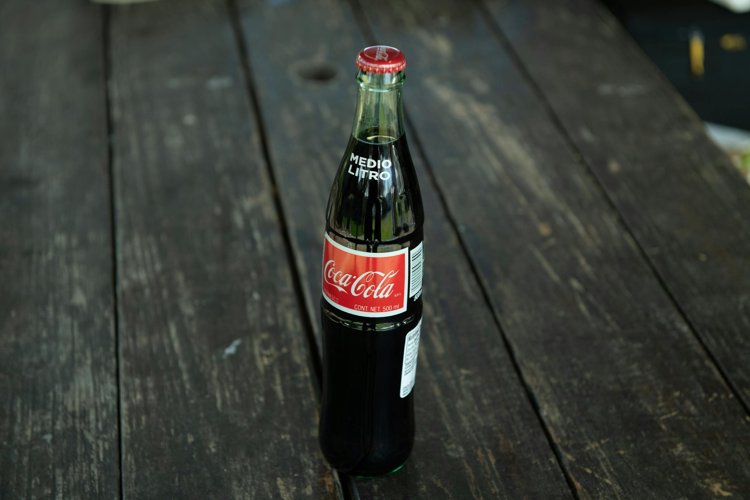 A classic Coca-Cola bottle placed on a rustic wooden table outdoors.