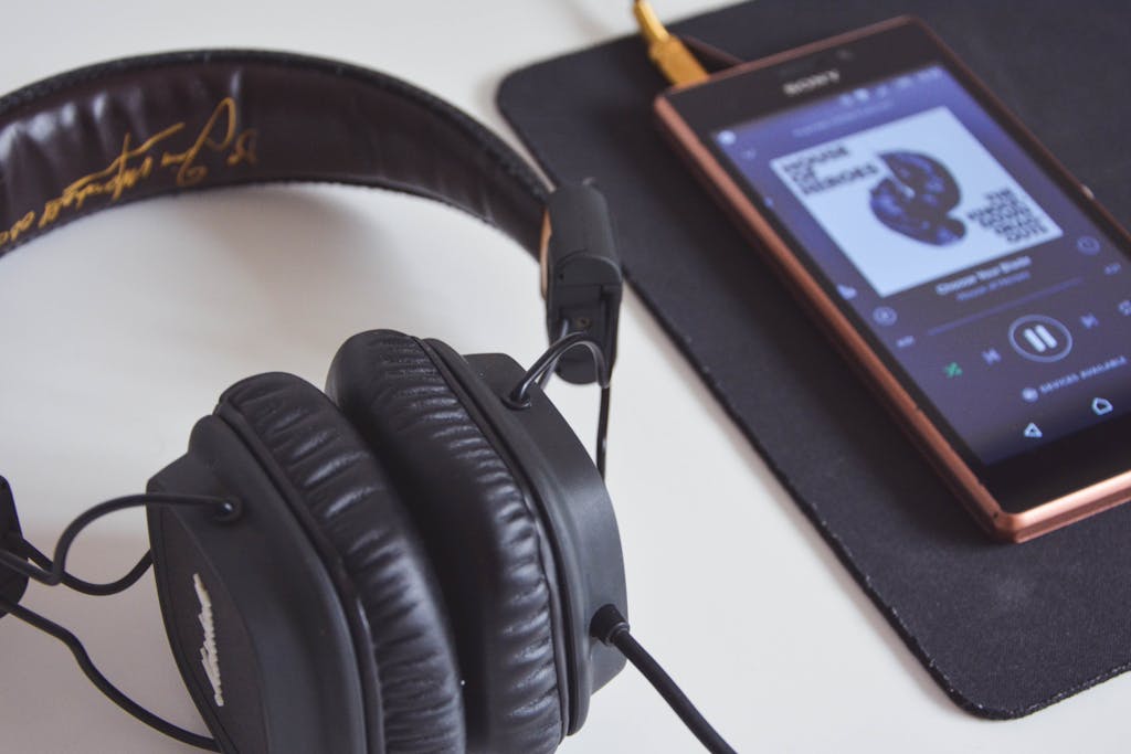 A close-up of headphones and a smartphone playing music on a desk.
