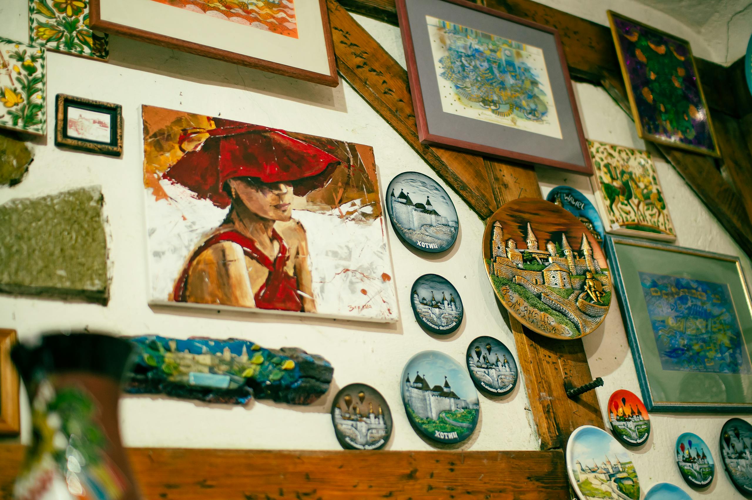 A collection of colorful paintings and decorative plates displayed creatively on a wooden wall.