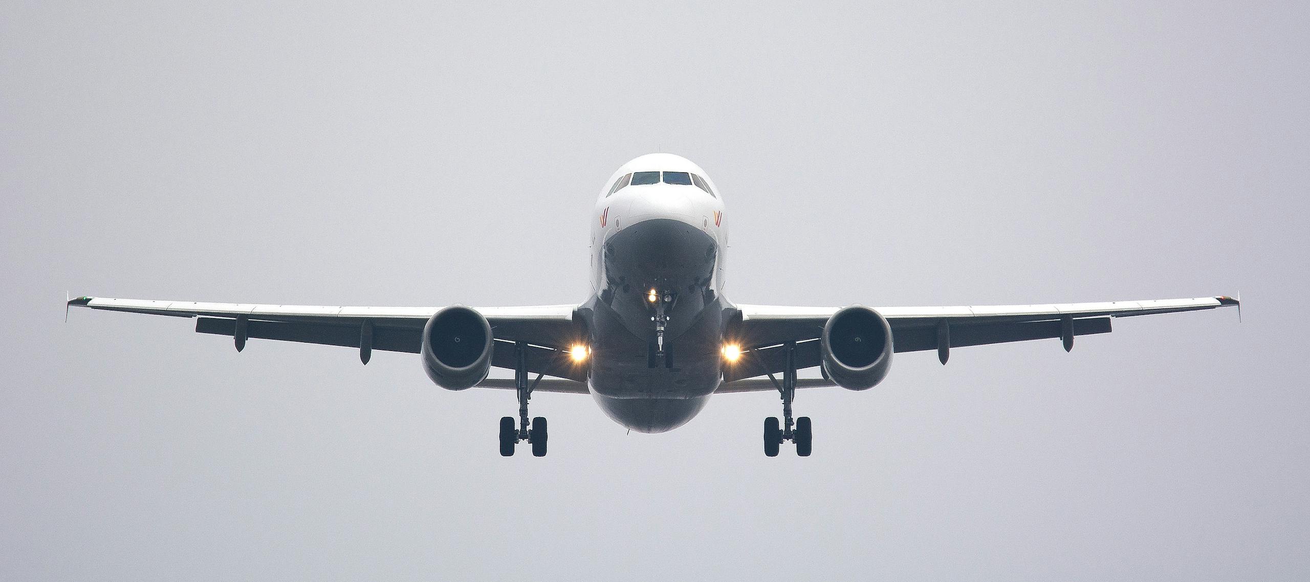 A commercial airliner captured head-on, preparing to land against a cloudy sky.