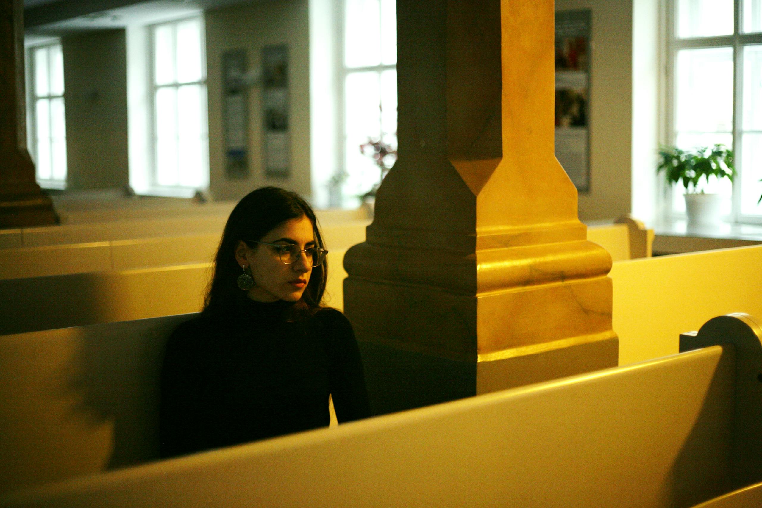 A contemplative woman sits alone in a church pew, evoking a sense of solitude.