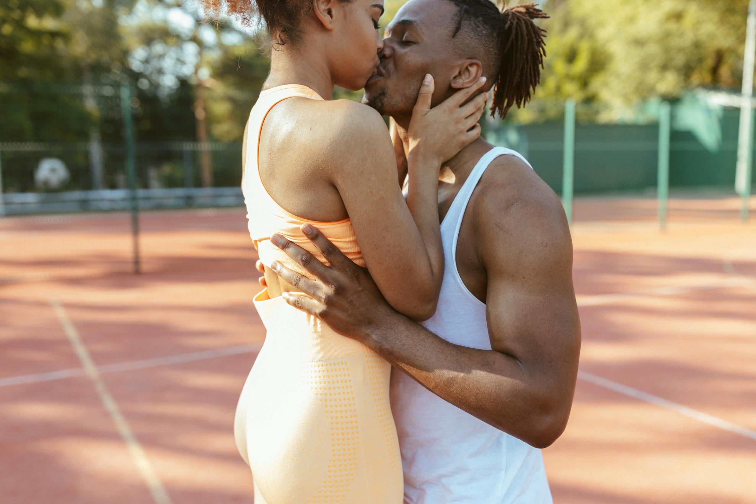 A couple embraces and kisses on an outdoor tennis court, showcasing love and affection.
