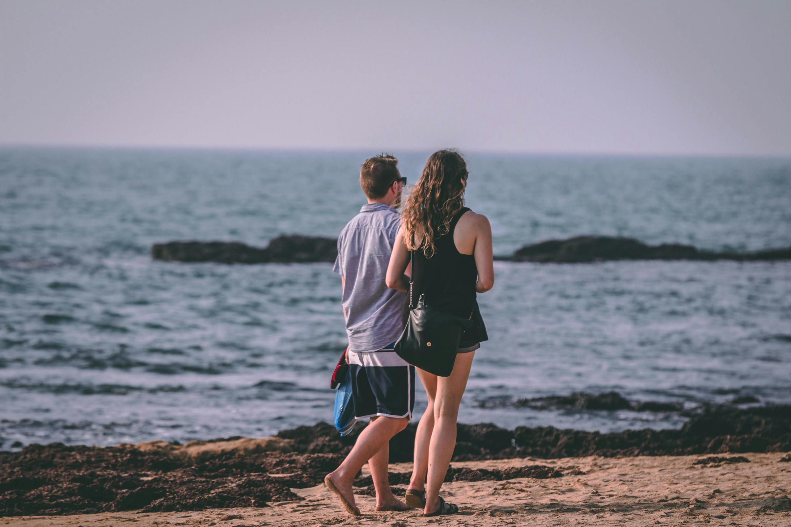 A couple enjoys a romantic walk on a sandy beach by the ocean, capturing leisure and love.