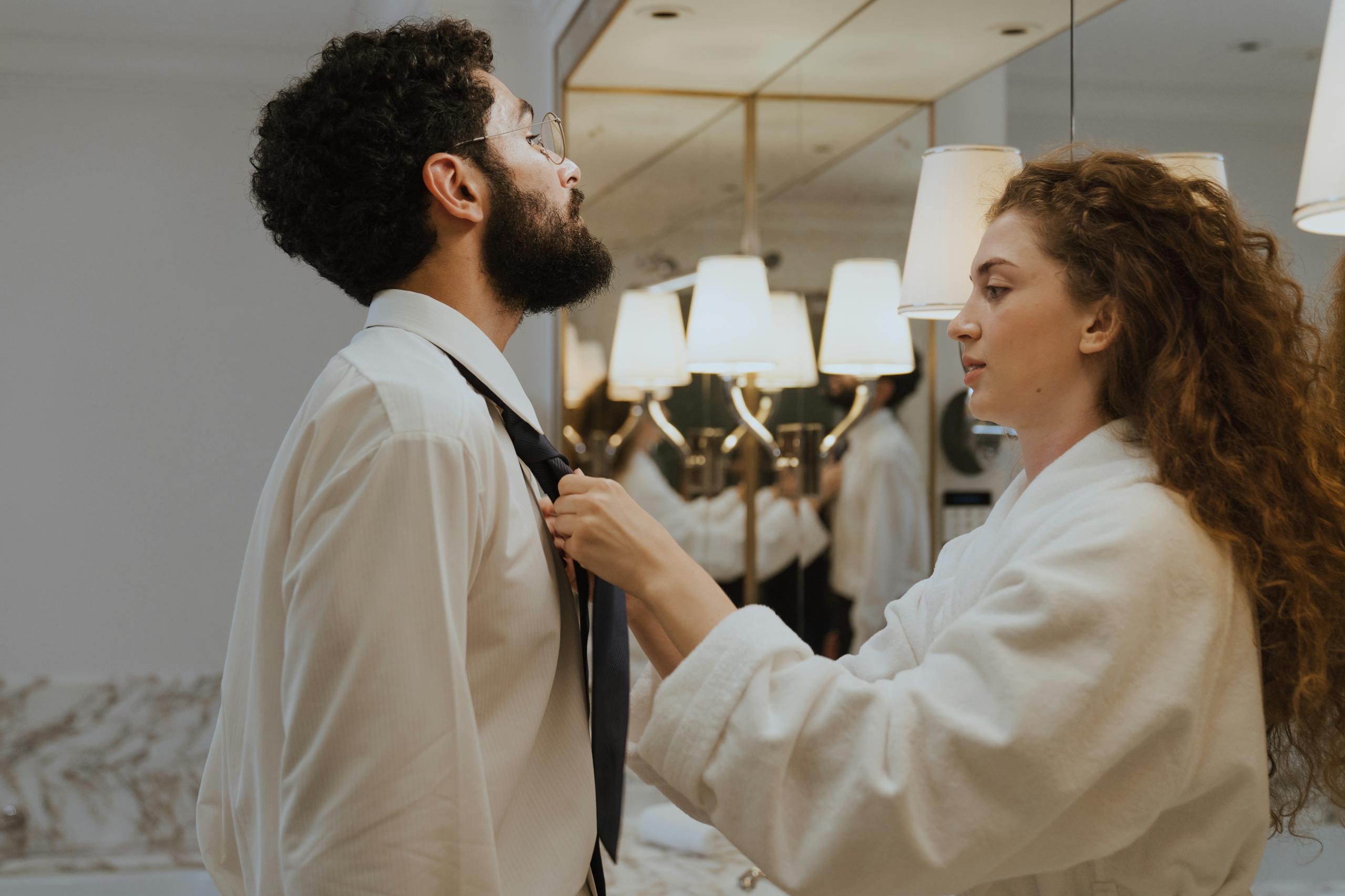 A couple in a bathroom, helping each other get ready for work, showcasing teamwork and togetherness.