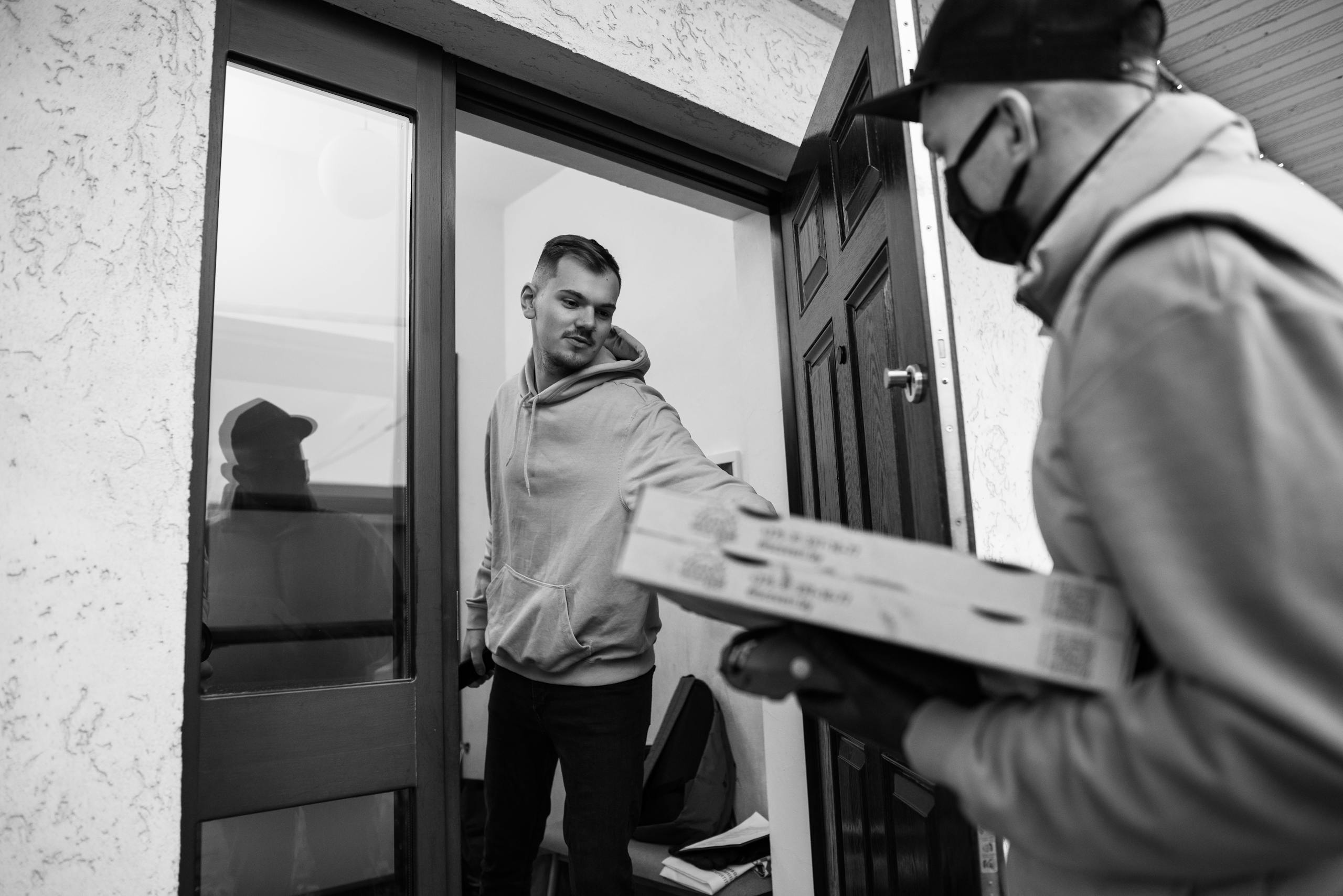 A deliveryman handing over pizza boxes to a customer at their doorstep, captured in monochrome.