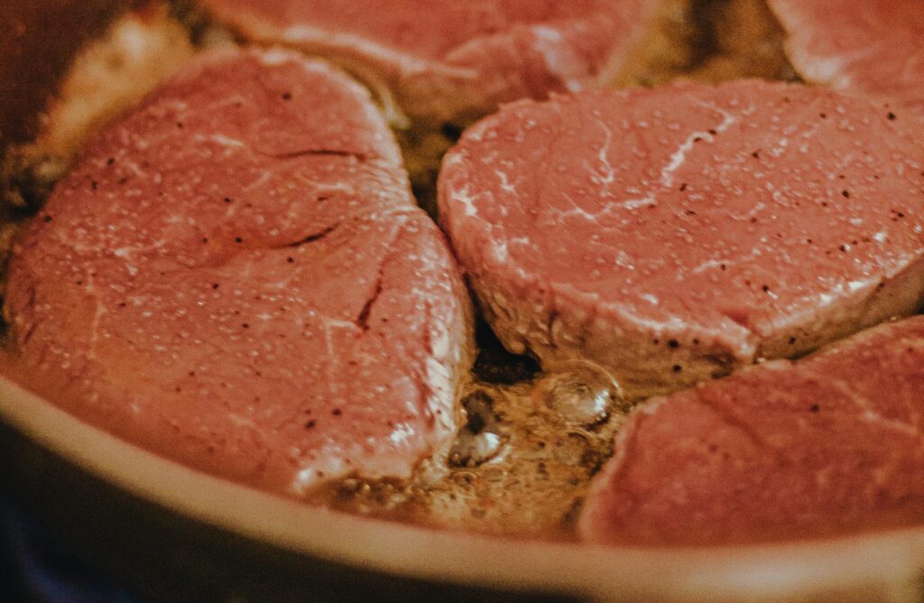 A detailed shot of raw beef slices sizzling in a copper frying pan, ready for cooking.