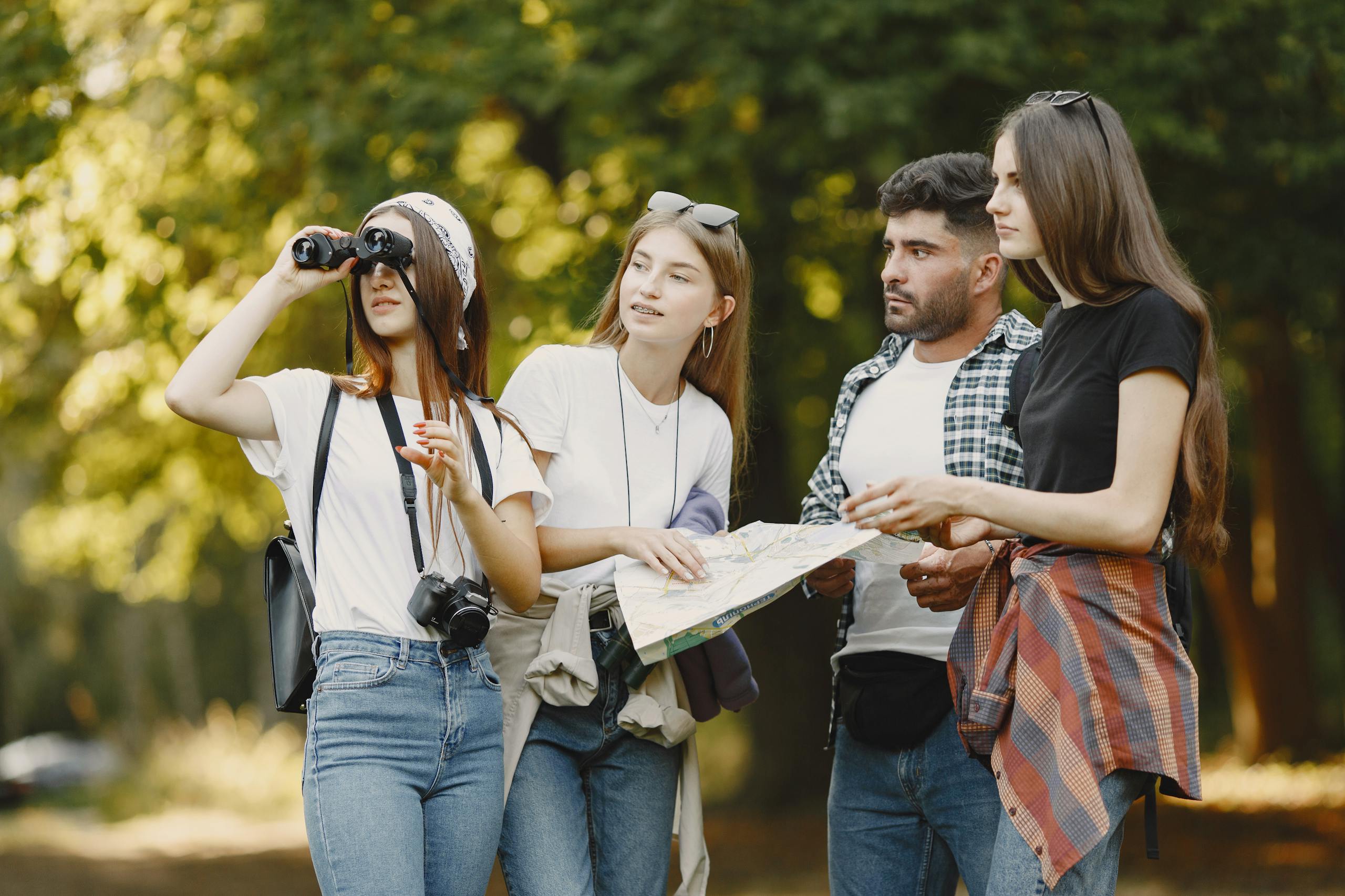 A diverse group of friends use a map and binoculars in a park, enjoying a sunny day outdoors.