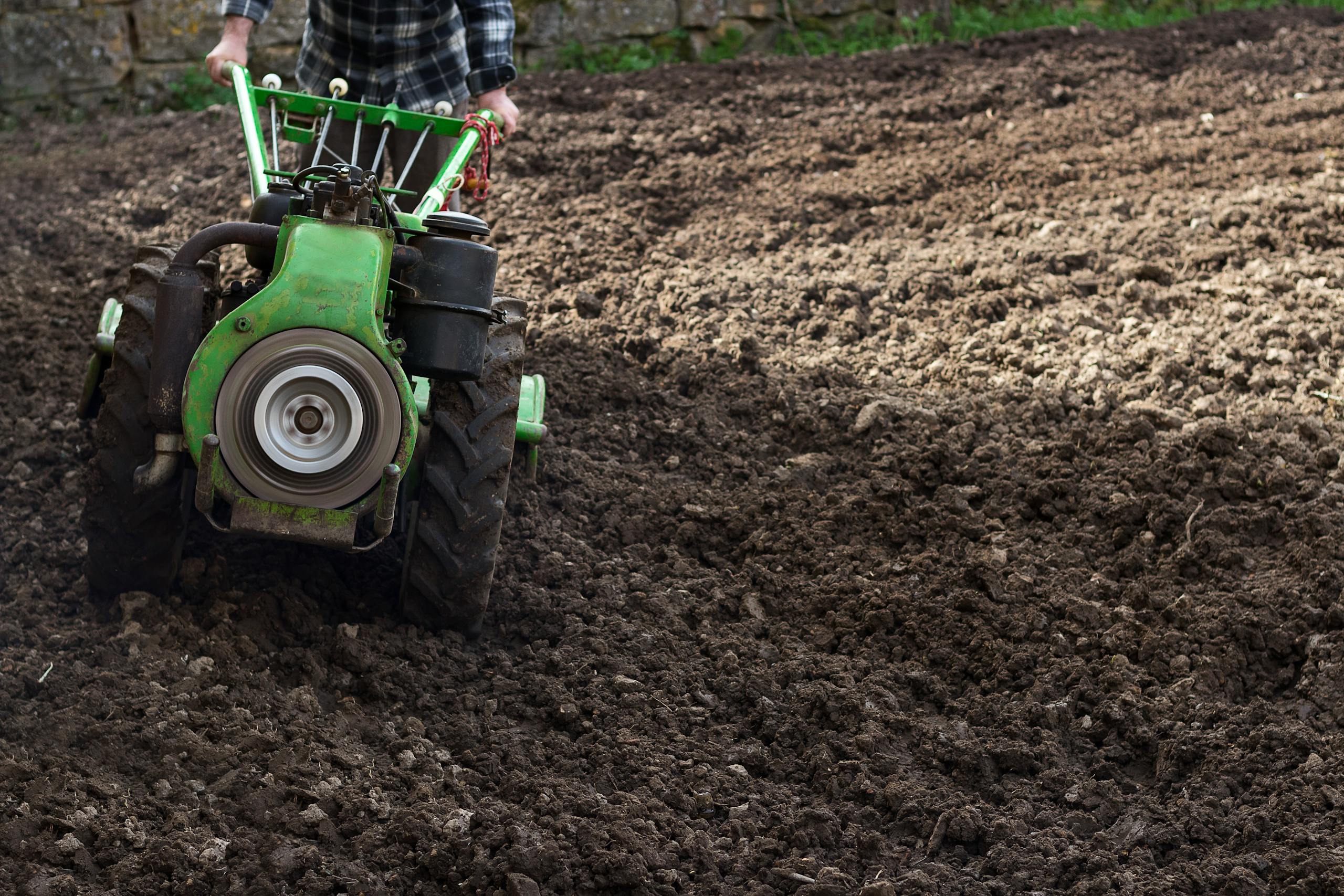 A farmer using a small green tractor to cultivate soil in a rural field.