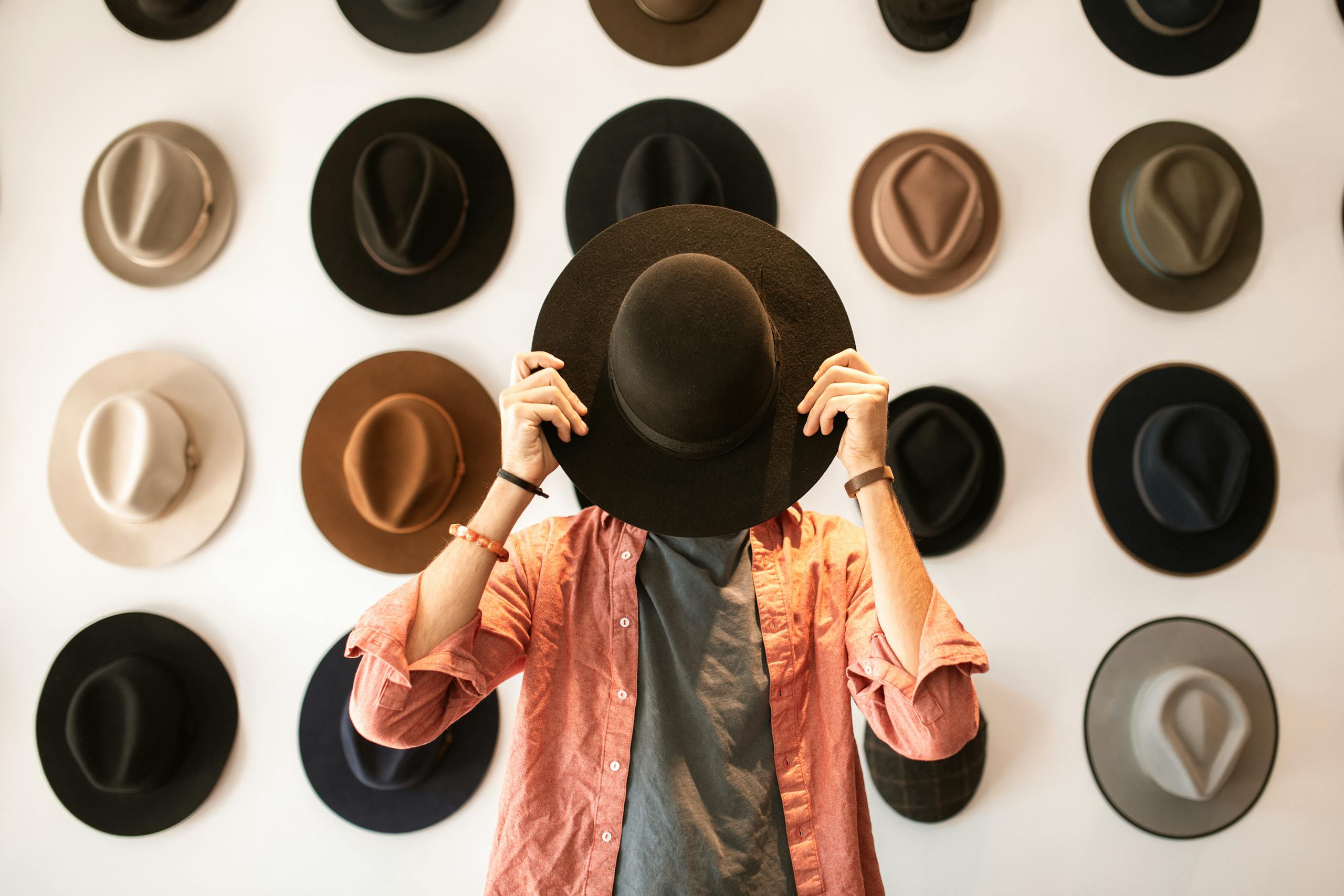 A fashionable individual holding a hat on a boutique wall of various hats.