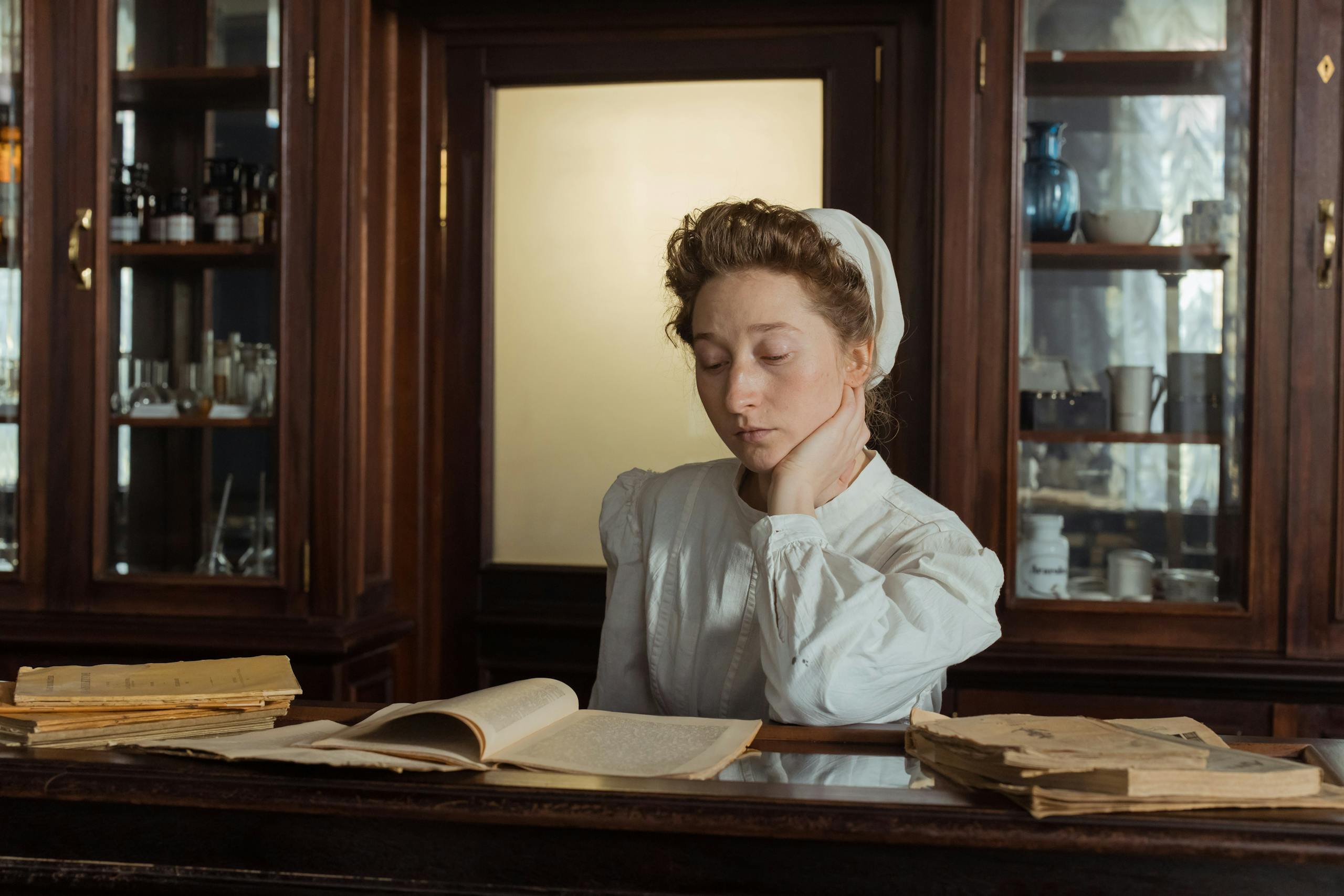 A female pharmacist in vintage attire reads in an old apothecary shop.