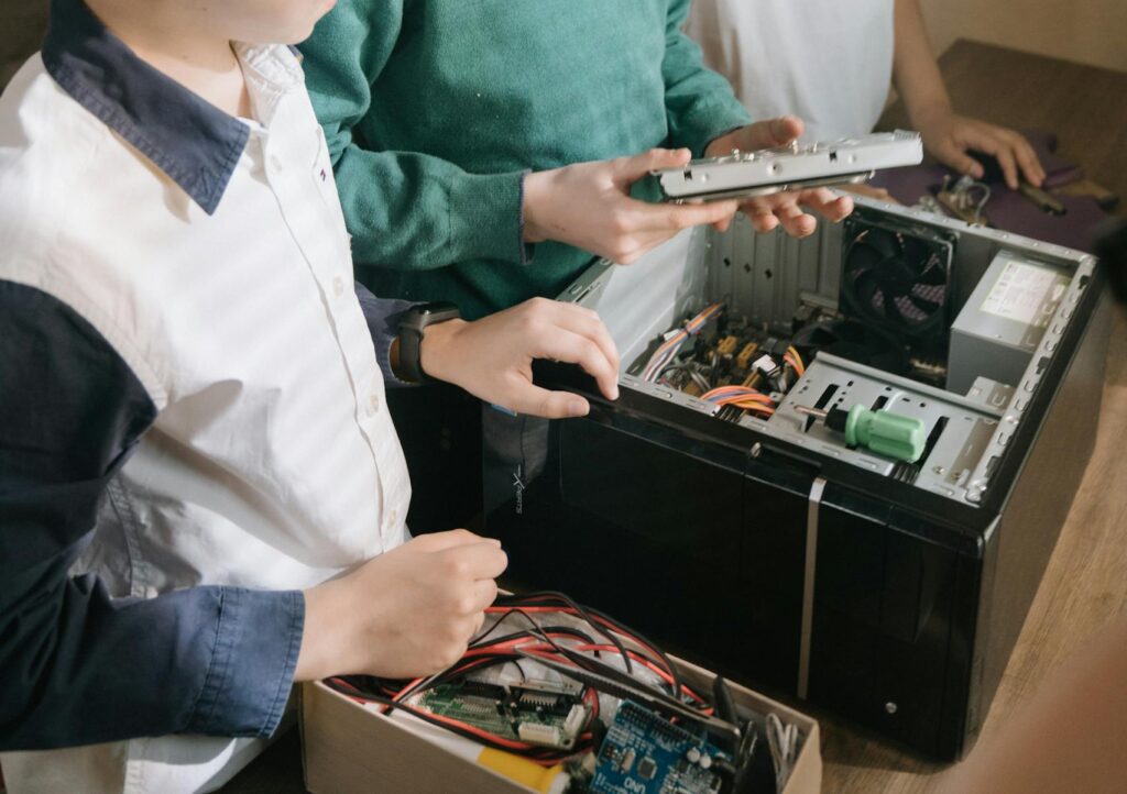 A group of young teenagers enthusiastically repairing a computer motherboard indoors.