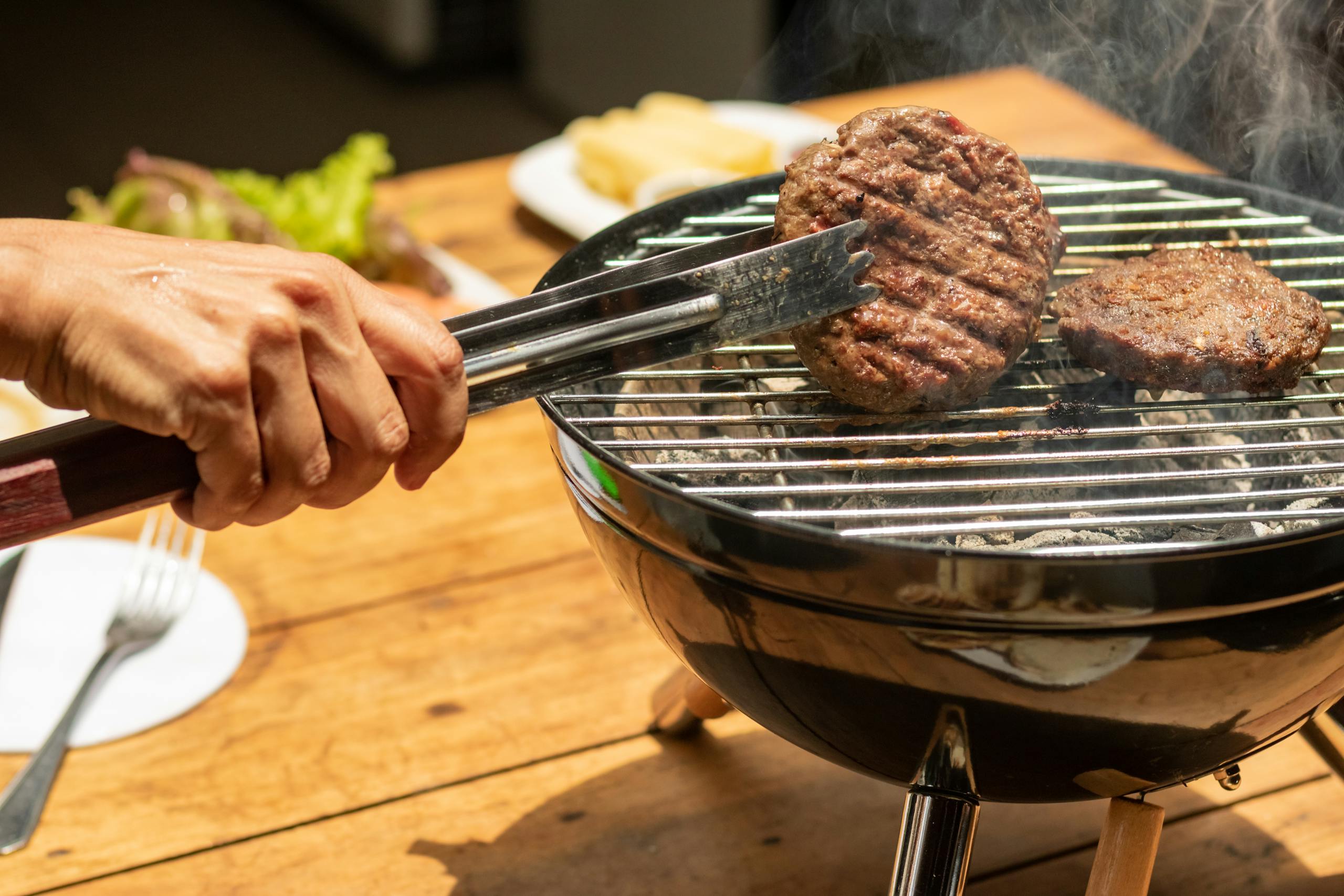 A hand uses tongs to grill burgers on a charcoal barbecue. Perfect for outdoor dining scenes.