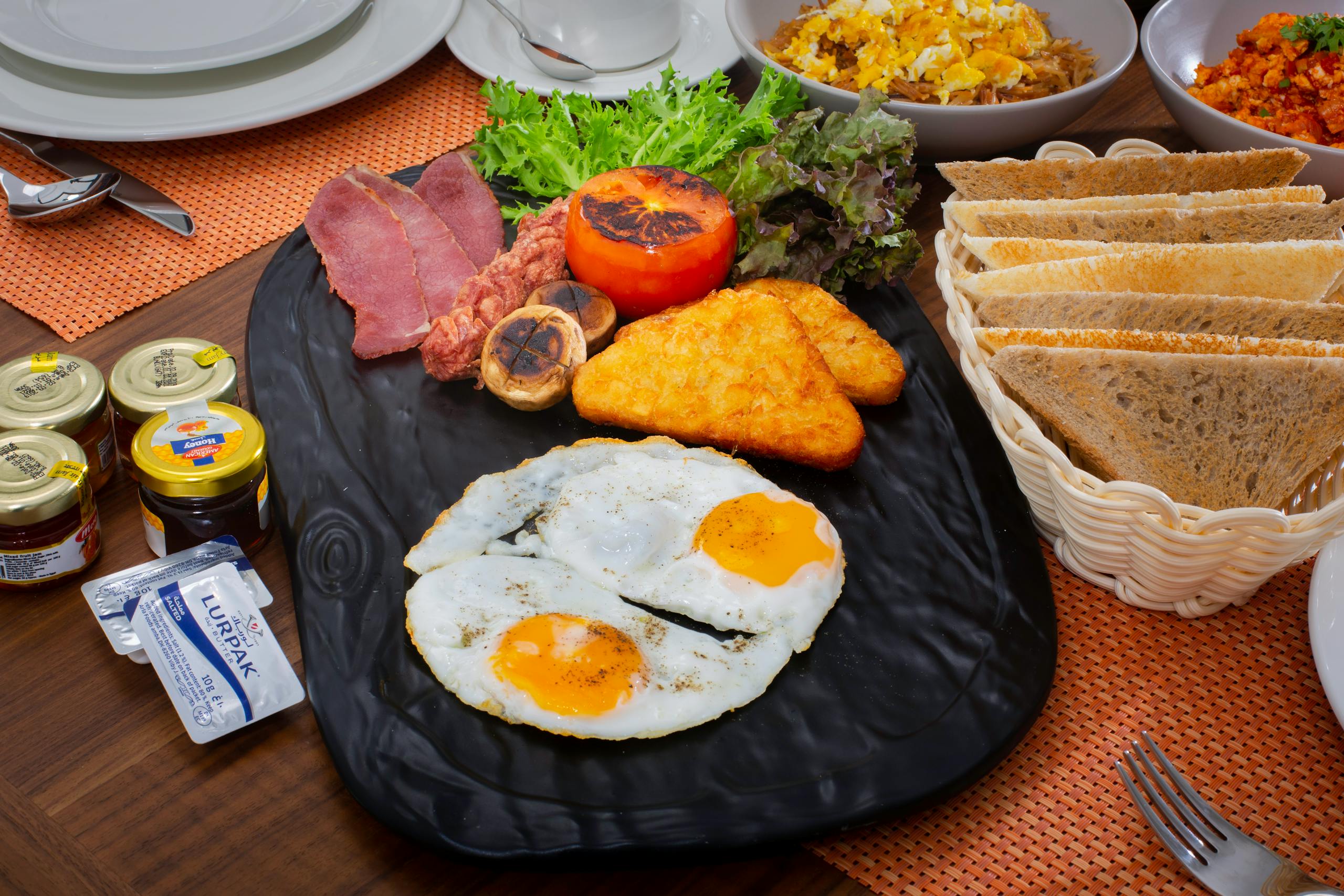 A hearty breakfast featuring eggs, bacon, toast, and more on a stylish stone plate.