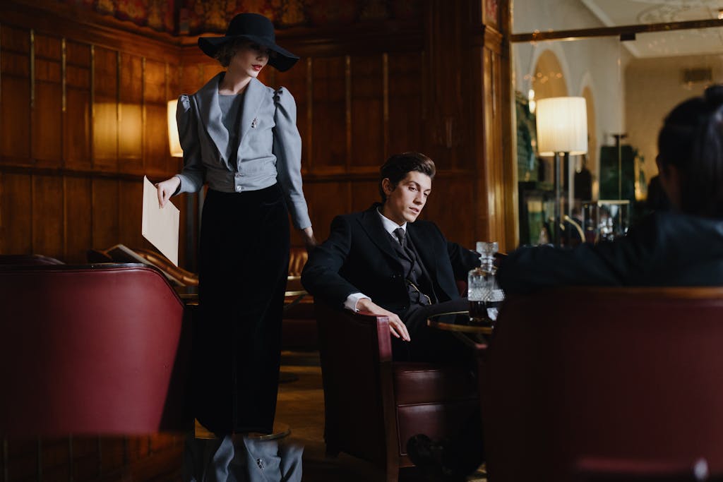 A man and woman in vintage attire converse in an elegant restaurant setting.
