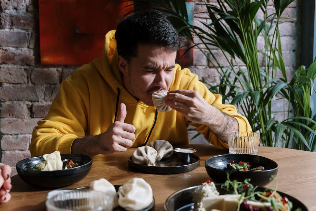 A man in a yellow hoodie savoring traditional Georgian dumplings, khinkali, indoors.