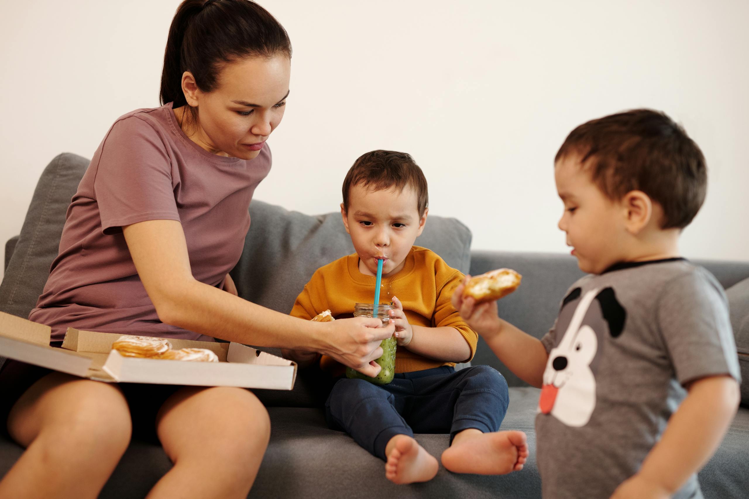 A mother and her twin boys share a snack on a cozy couch, highlighting family bonding.