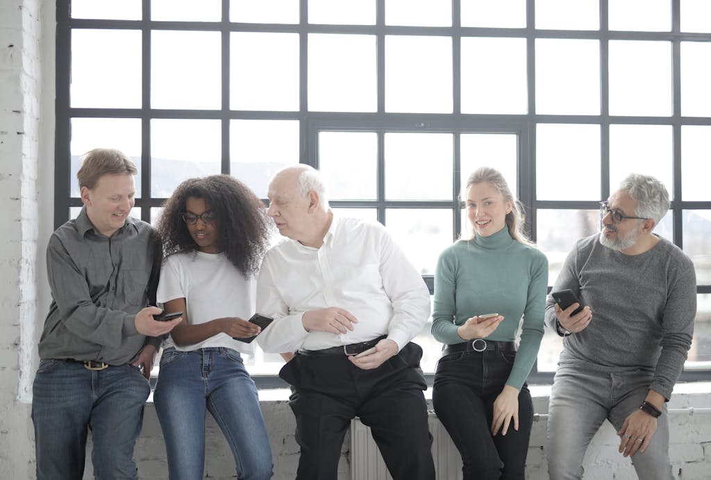A multicultural group of colleagues sitting indoors sharing smartphones creating a friendly team atmosphere.