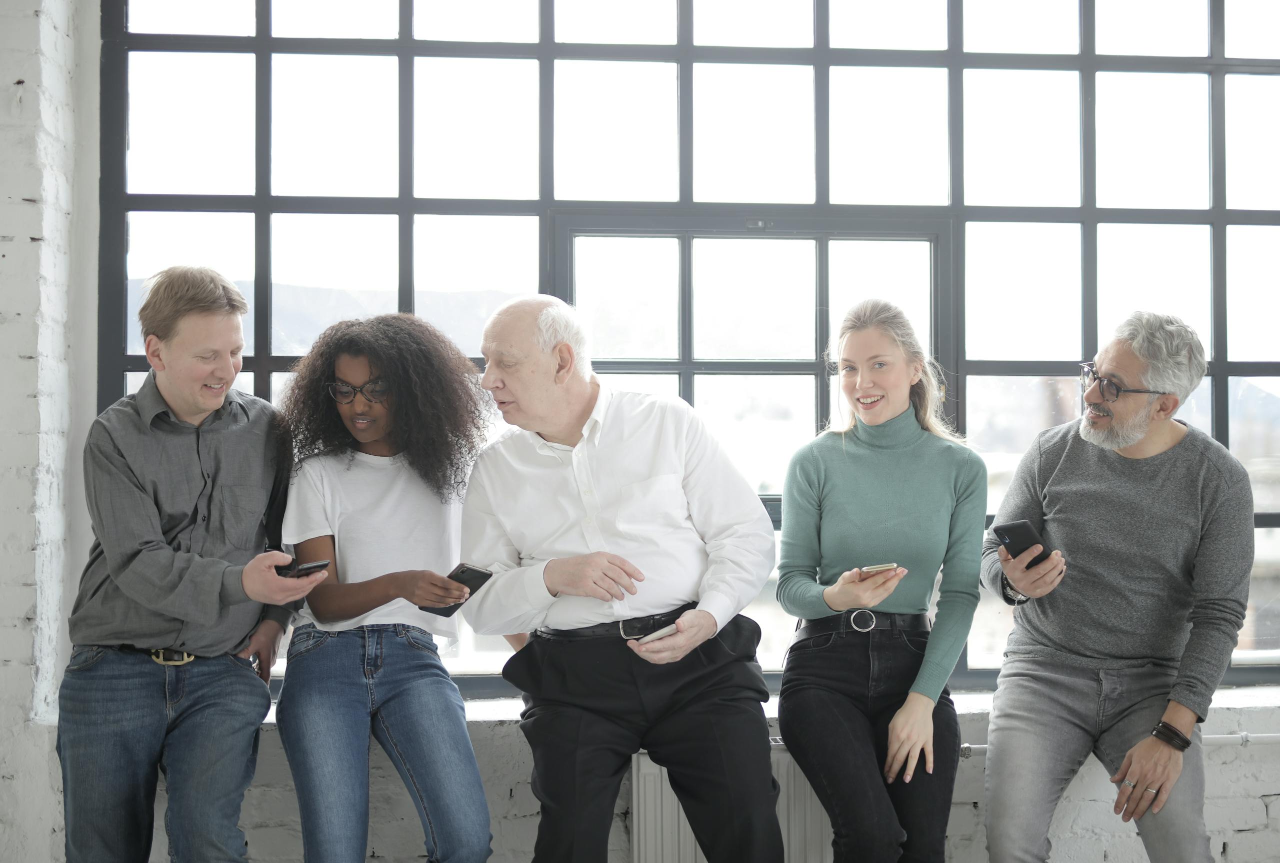 A multicultural group of colleagues sitting indoors sharing smartphones creating a friendly team atmosphere.