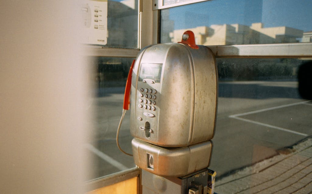 A nostalgic view of a vintage payphone in a sunlit urban street corner.