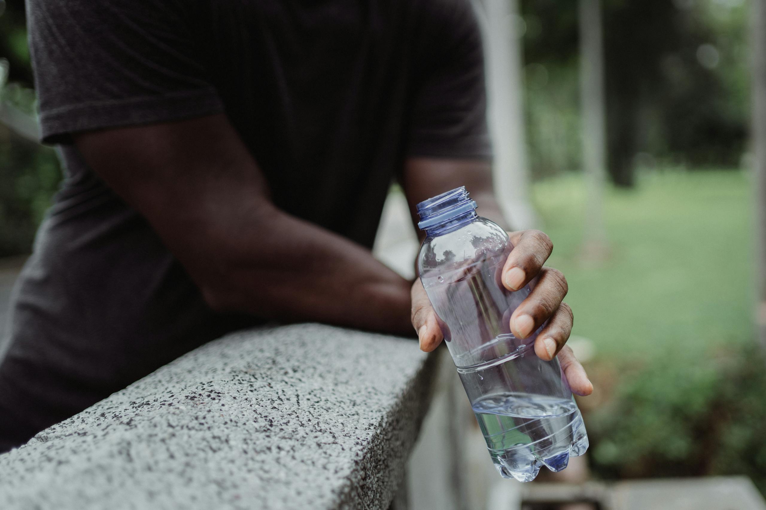 A person holds a plastic water bottle on a concrete rail outdoors, emphasizing hydration.