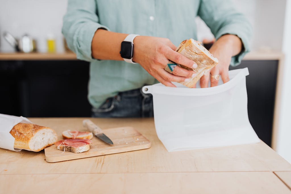 A person packs a sandwich into a silicone bag on a kitchen counter, highlighting eco-friendly food storage.