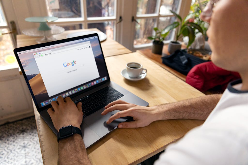 A person uses a laptop for internet browsing. A bright indoor setting with coffee on a wooden table.