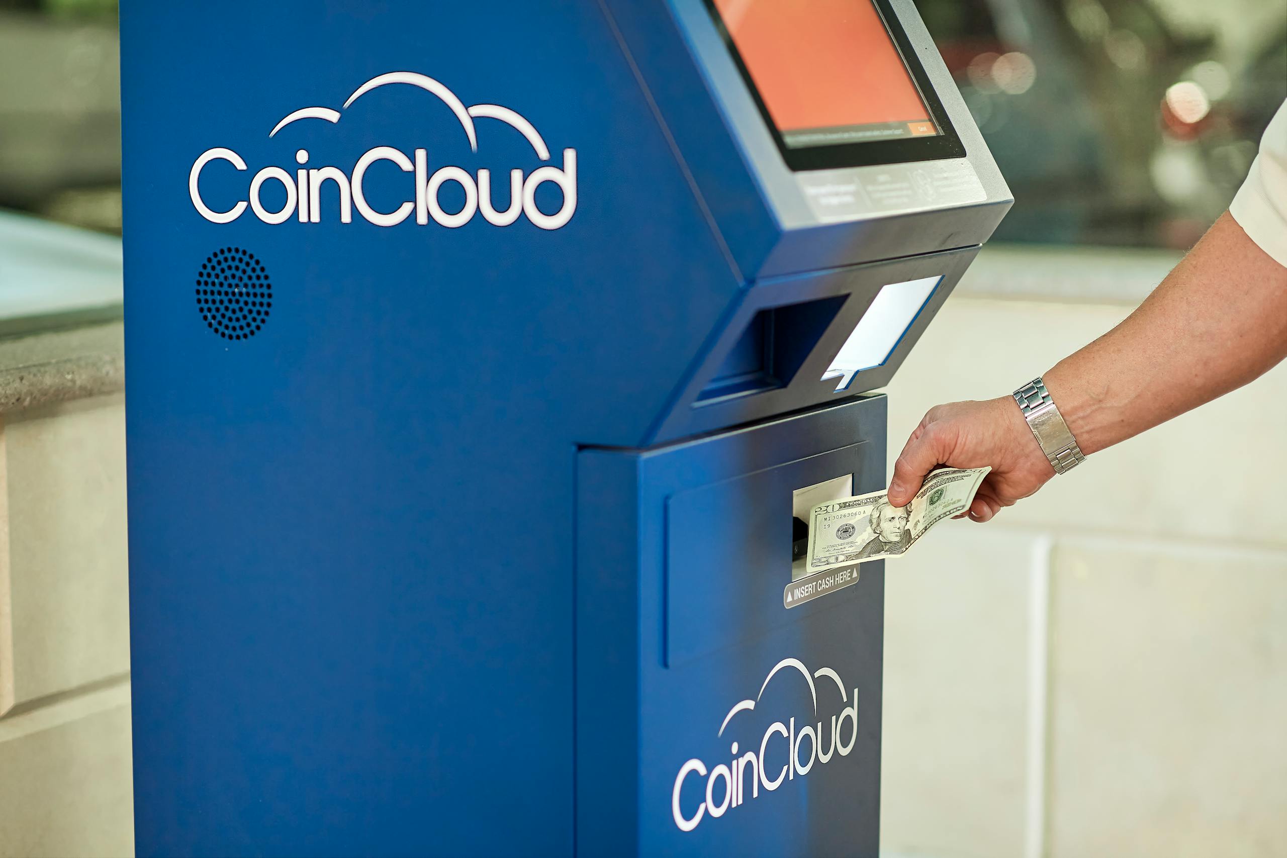 A person using a CoinCloud Bitcoin ATM to insert cash for cryptocurrency transactions.