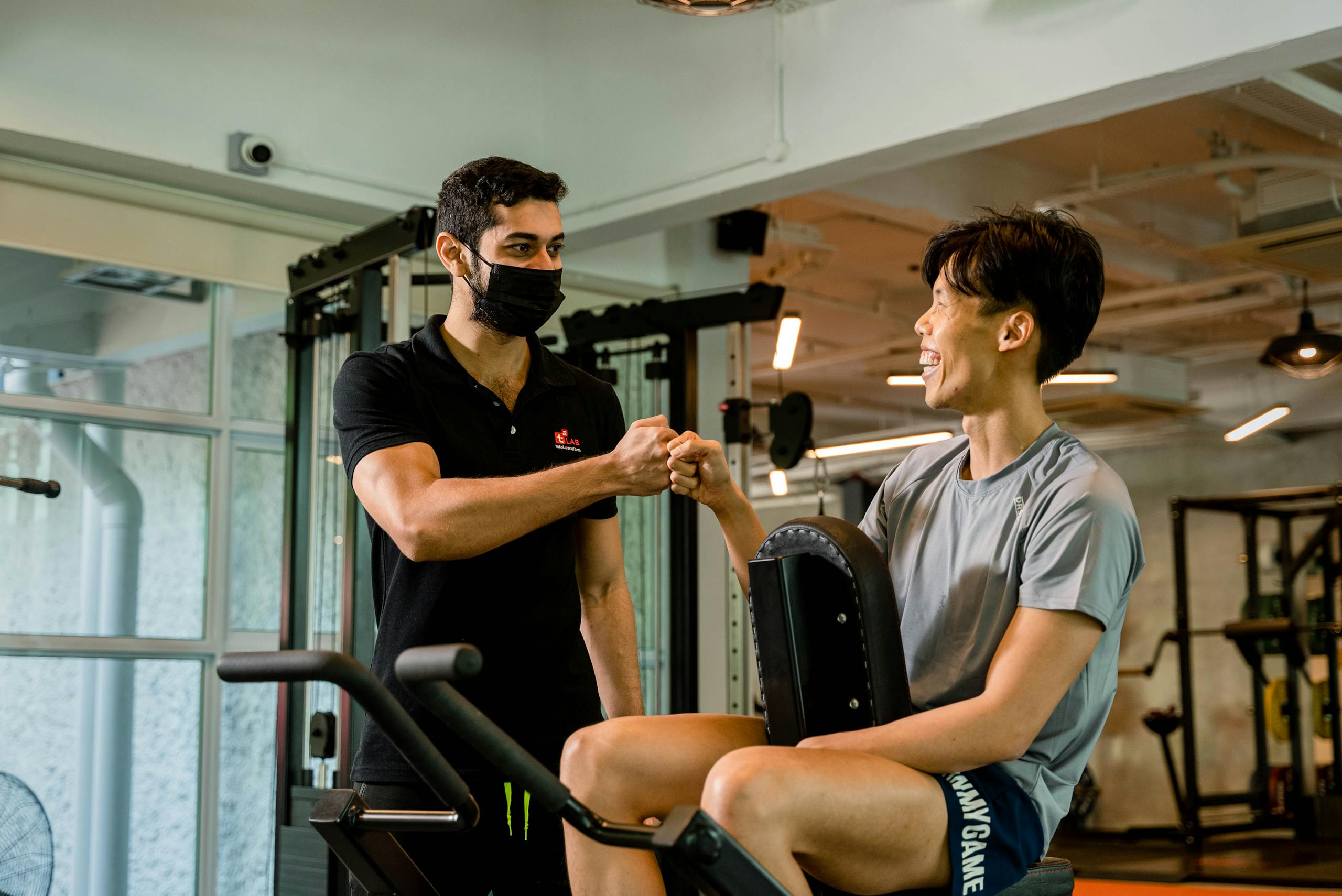 A personal trainer fist bumps a smiling client, promoting fitness motivation in a Singapore gym.