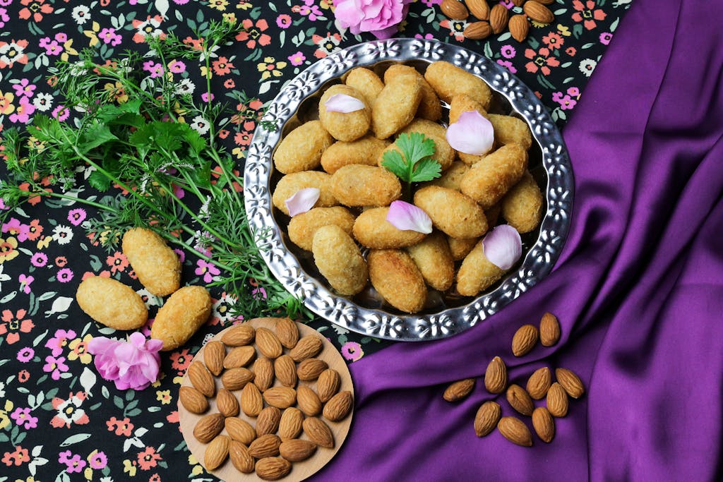 A plate of golden-brown fried snacks garnished with parsley and surrounded by almonds on a floral tablecloth.