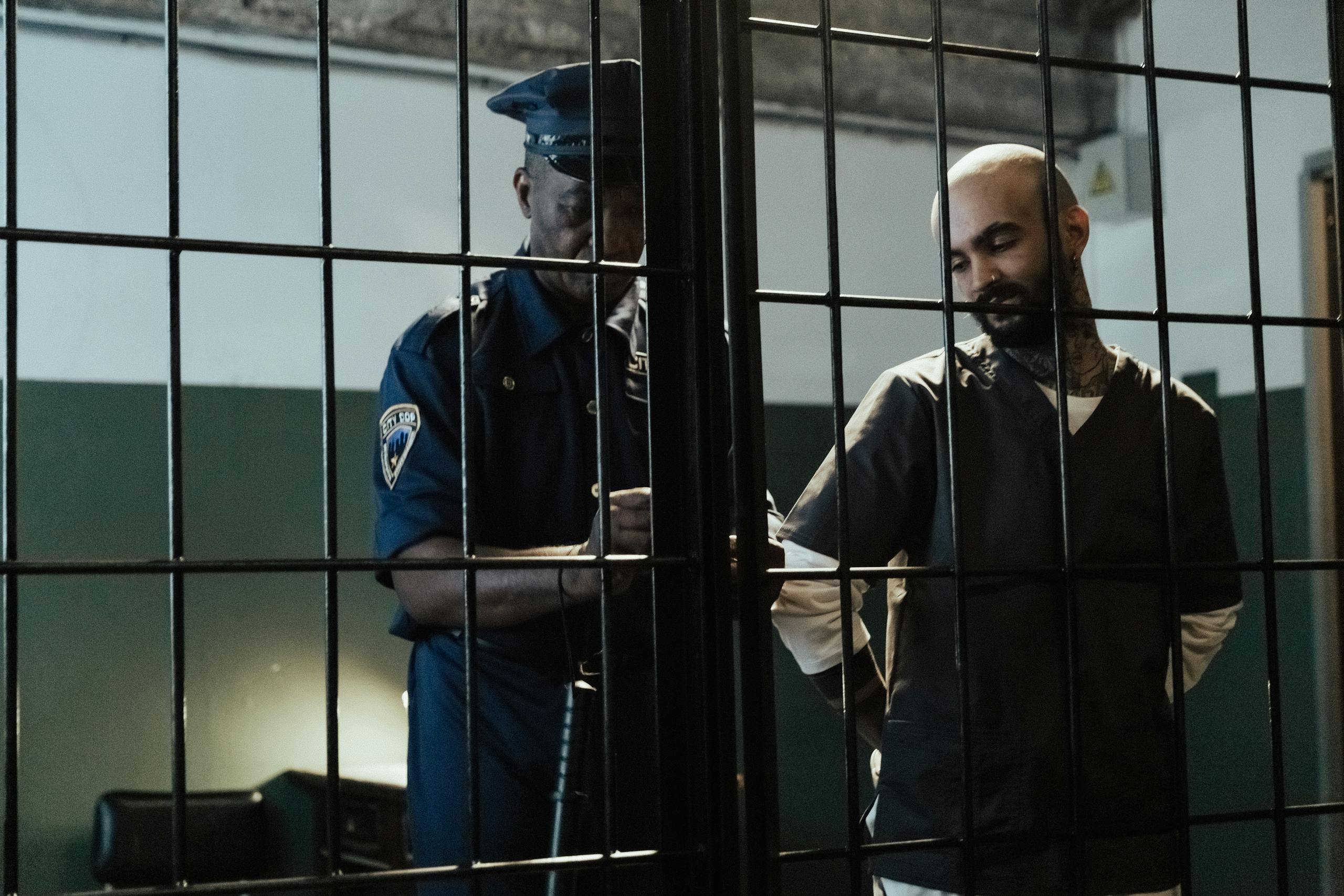 A policeman arrests a bald man in a dimly lit prison cell, conveying confinement.