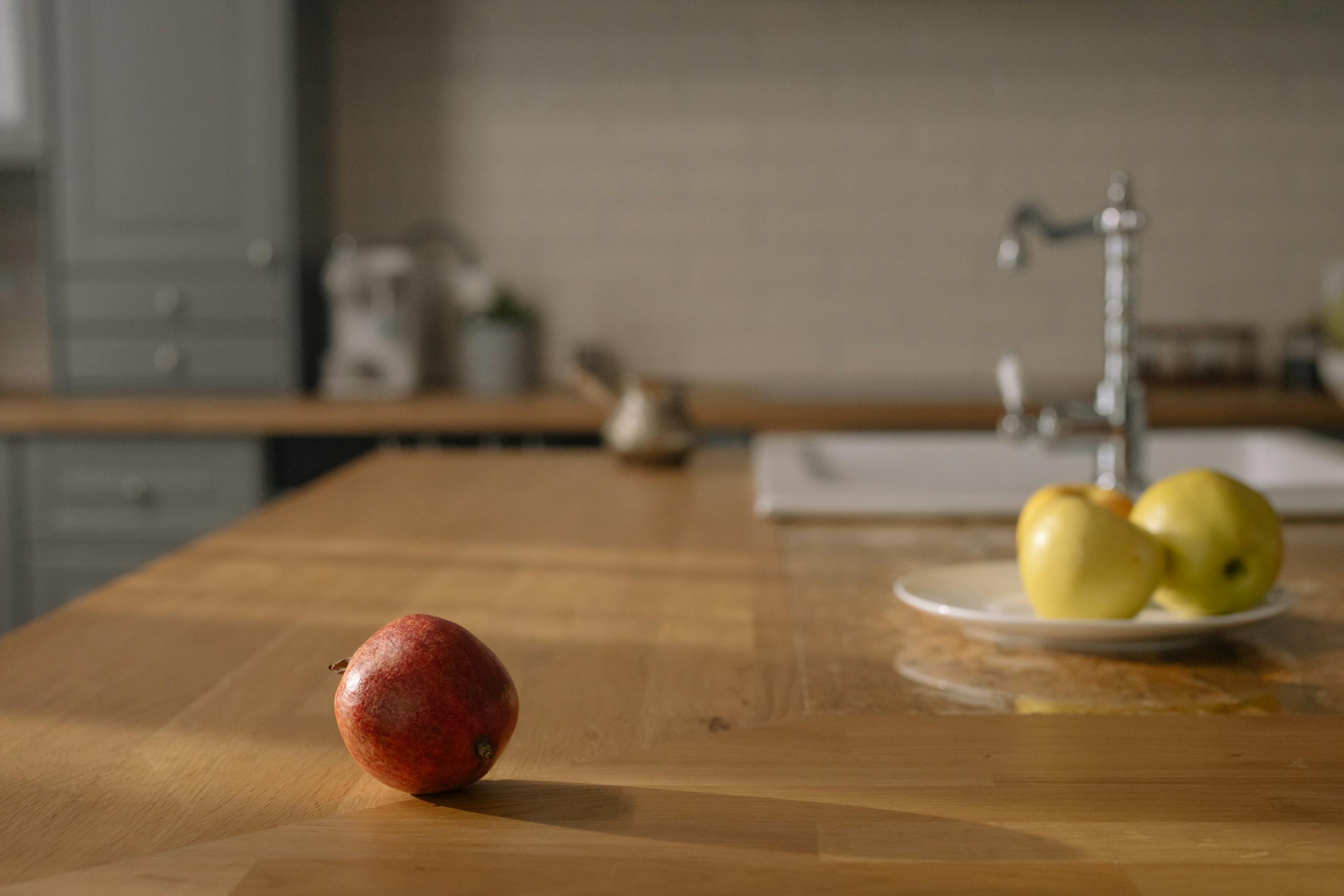 A red apple on a wooden counter and yellow apples on a plate in a cozy kitchen.