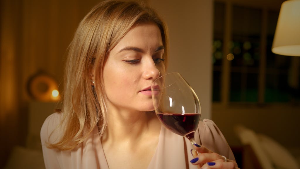 A relaxed woman savors a glass of red wine in a cozy indoor setting.