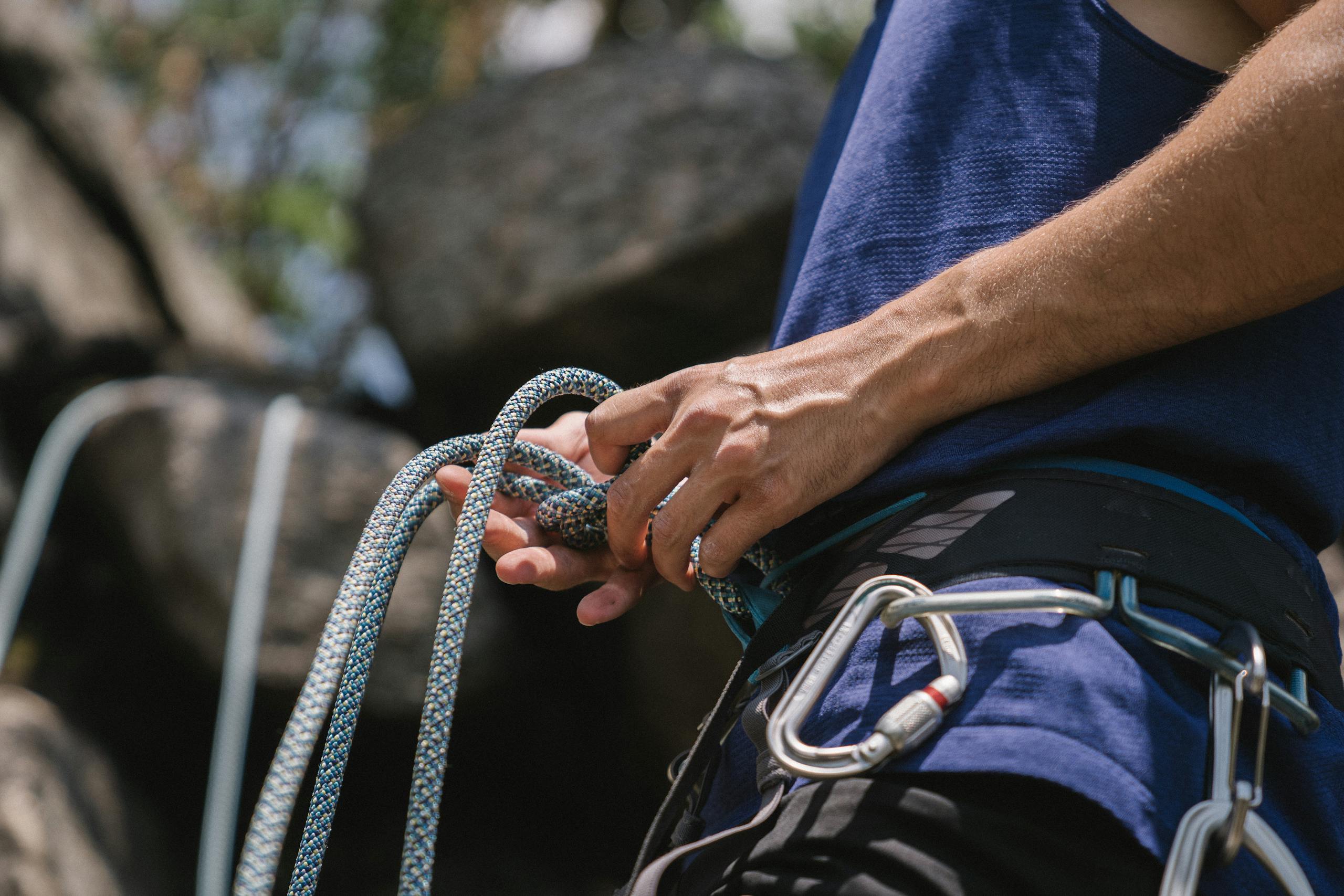 A rock climber tying knots and preparing safety gear for a climb outdoors.